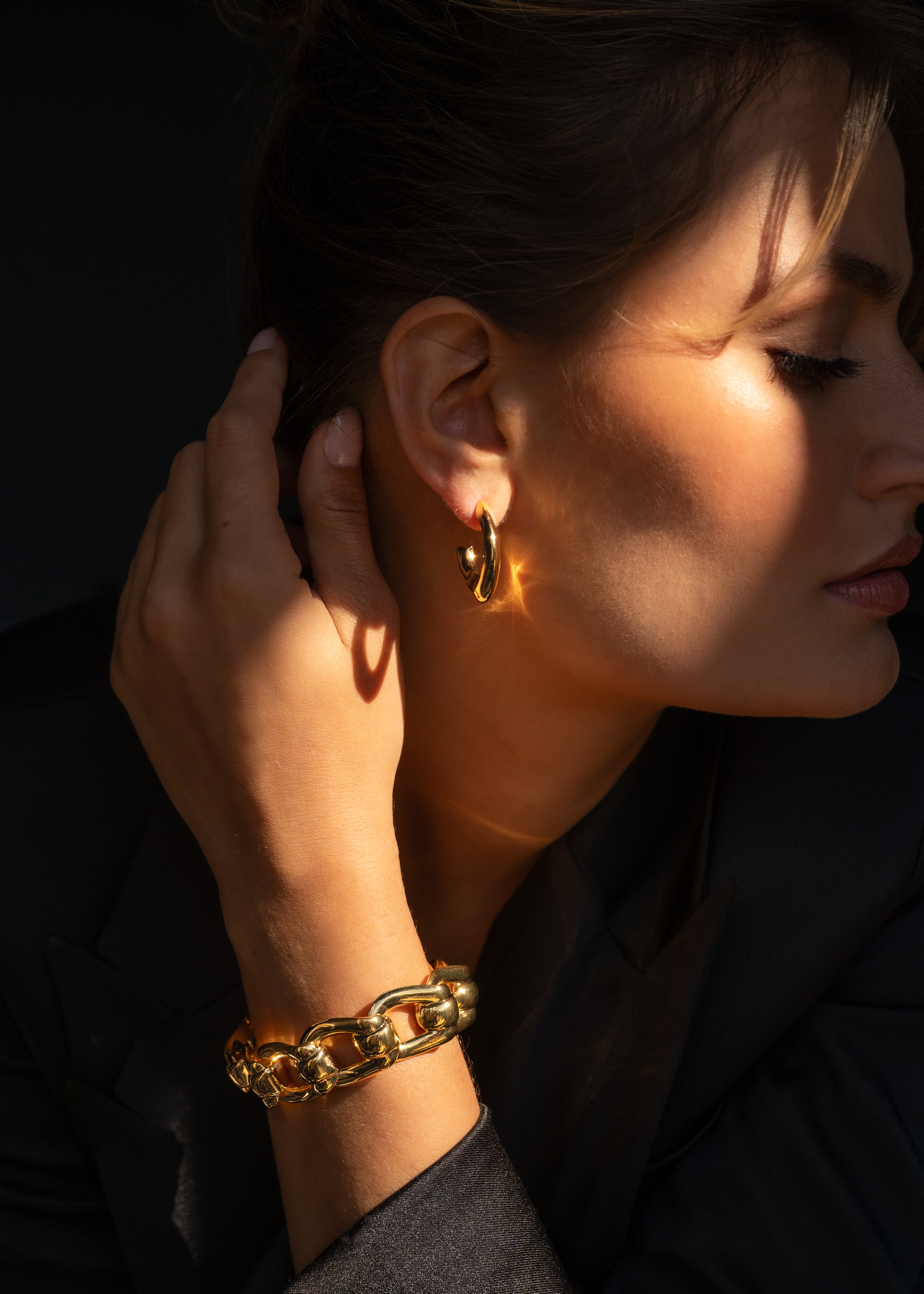 wearing gold earrings and bracelet against a dark background