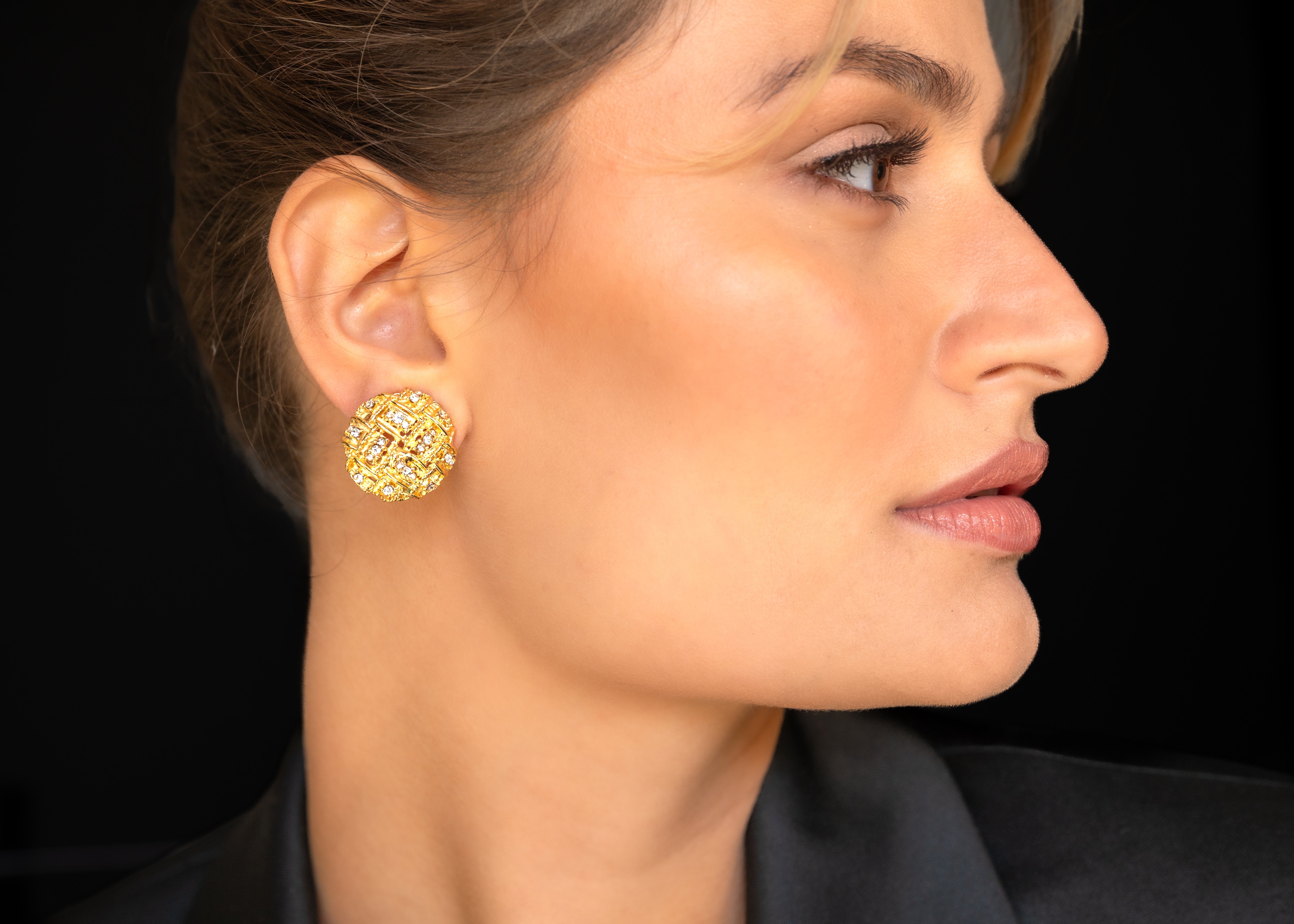 Close-up of a woman wearing gold earrings against a black background