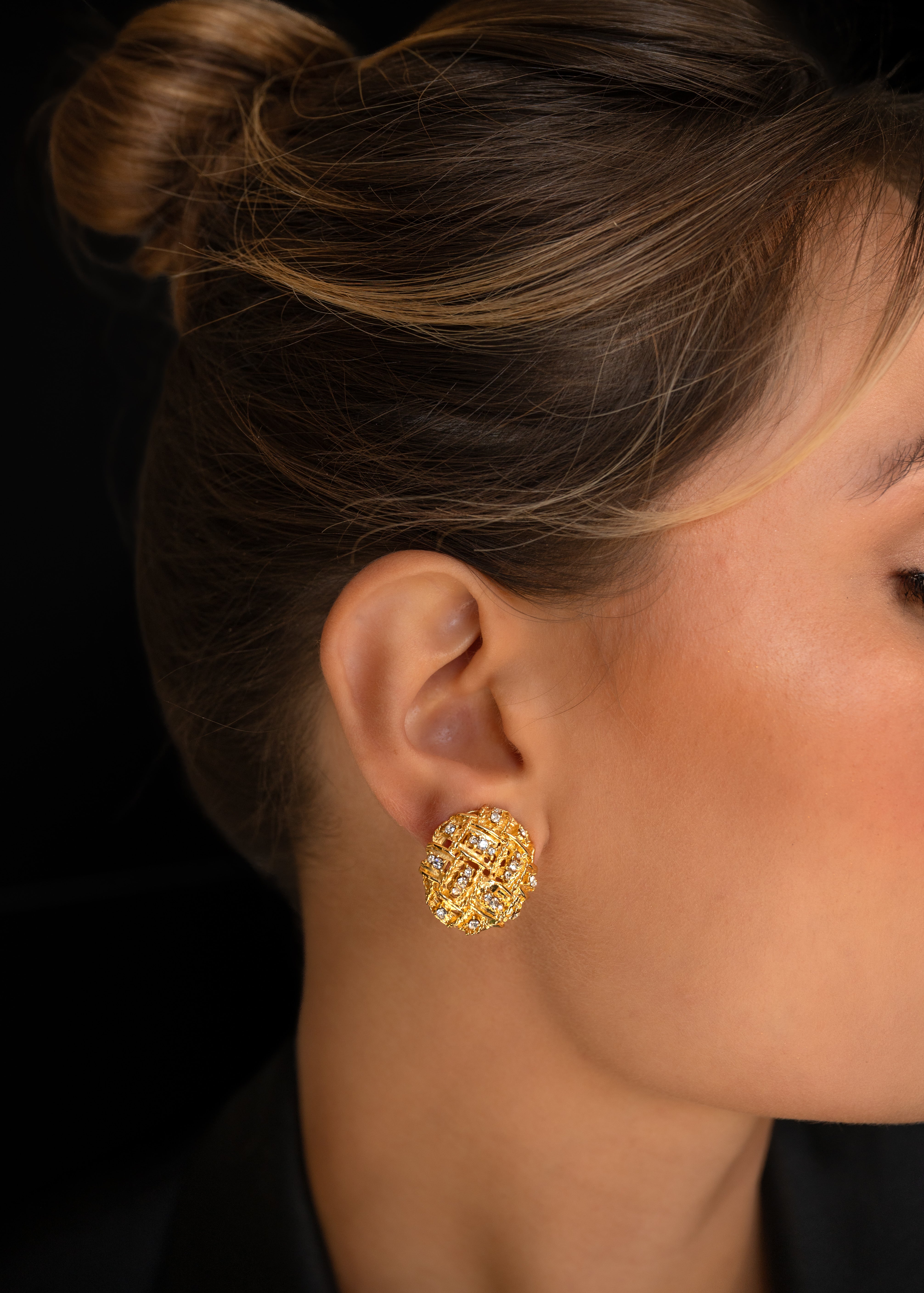 Close-up of a person wearing gold earrings against a black background