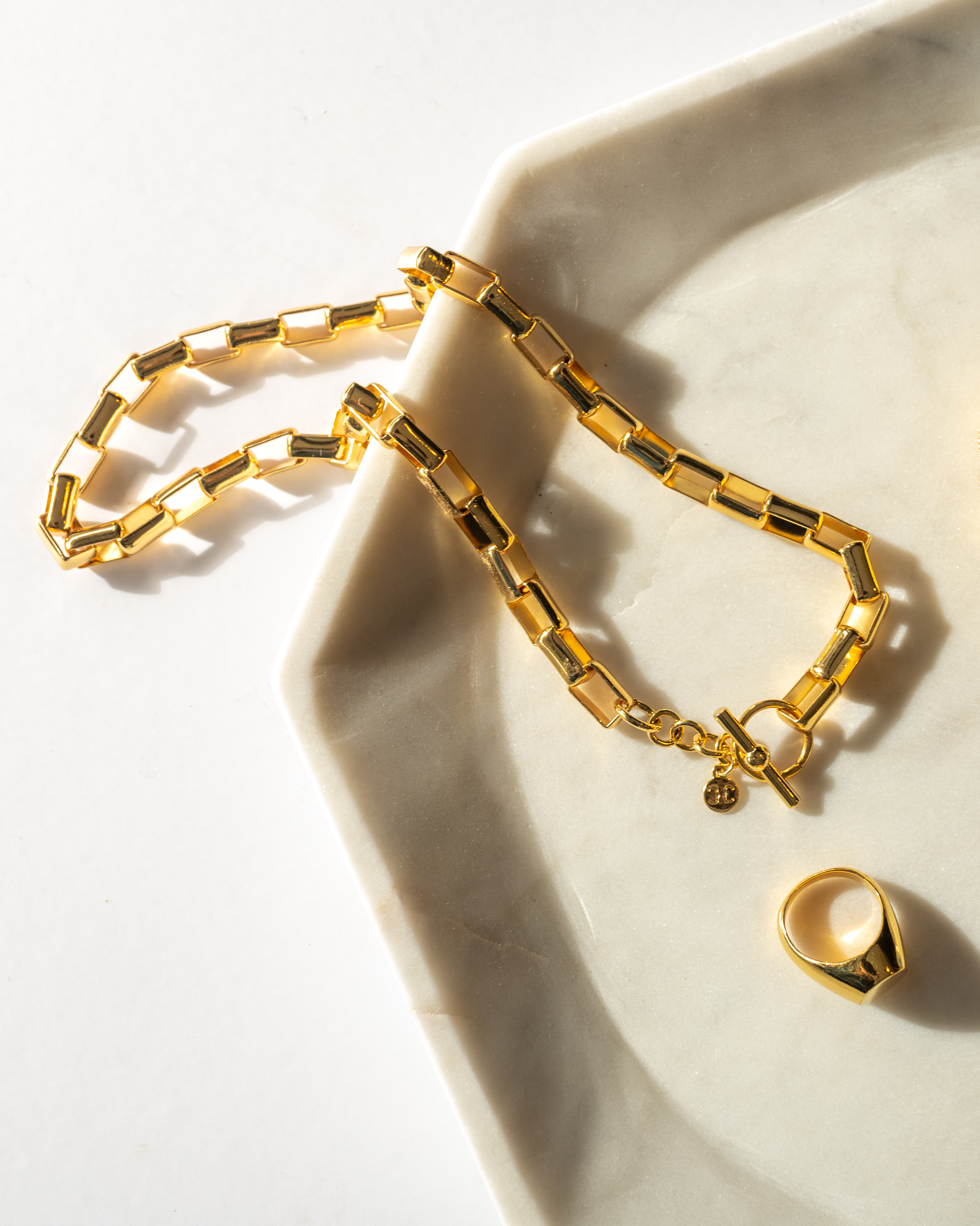 Box Link Necklace laying on a marble plate with a matching gold ring